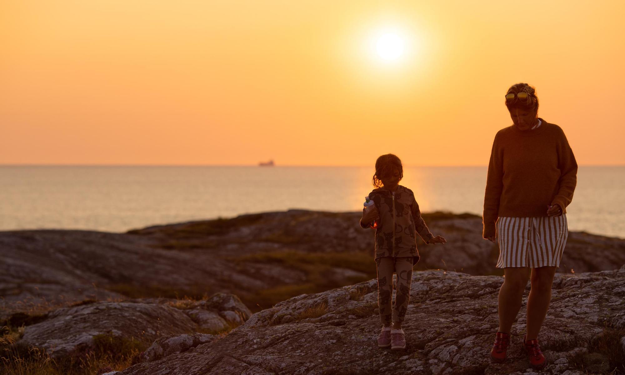 Barn och mamma som promenerar på klipporna i solnedgången